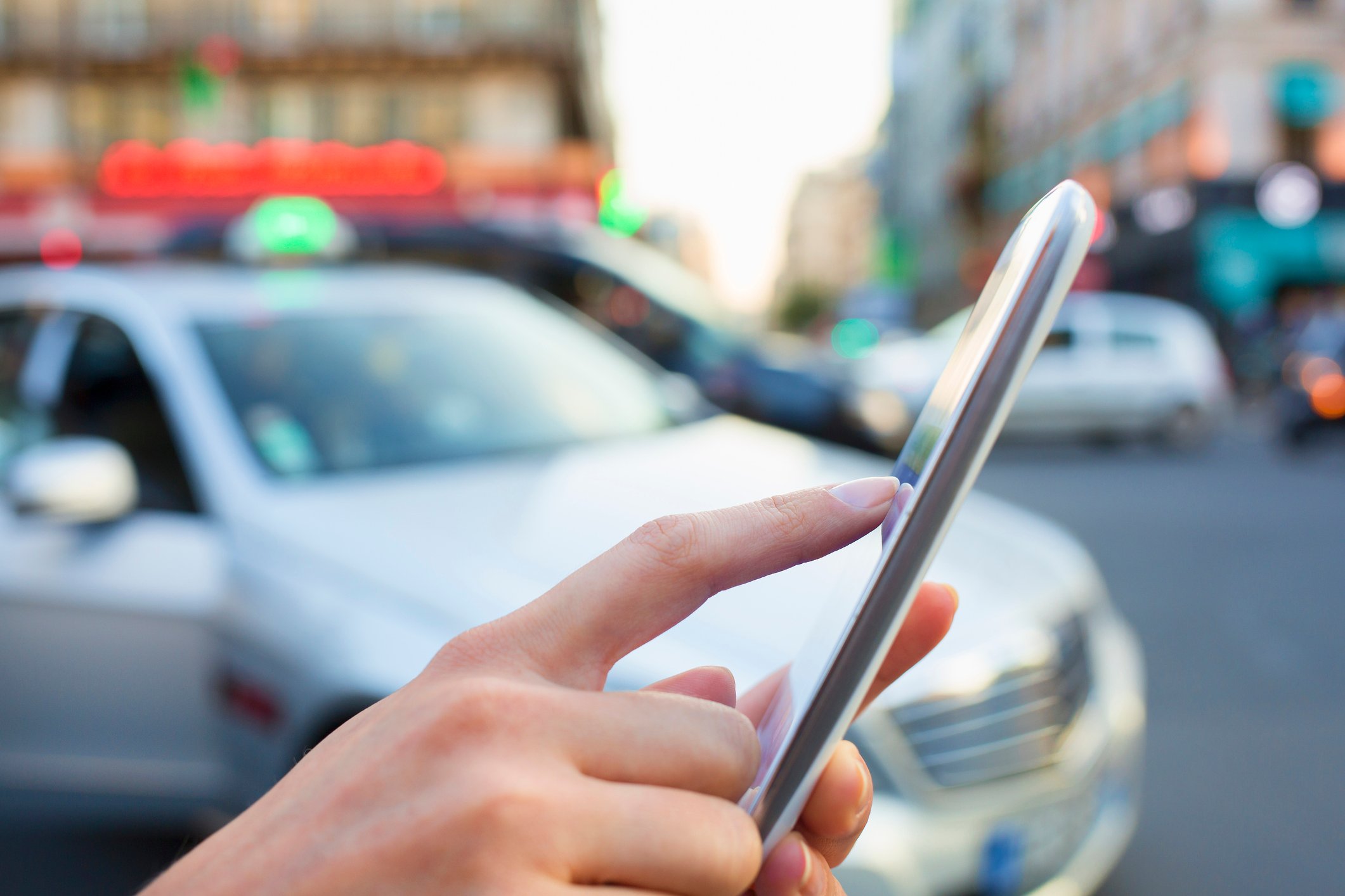 A person touching a smartphone's screen while a car is parked nearby