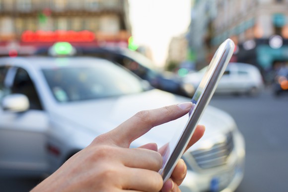 A person touching a smartphone's screen while a car is parked nearby