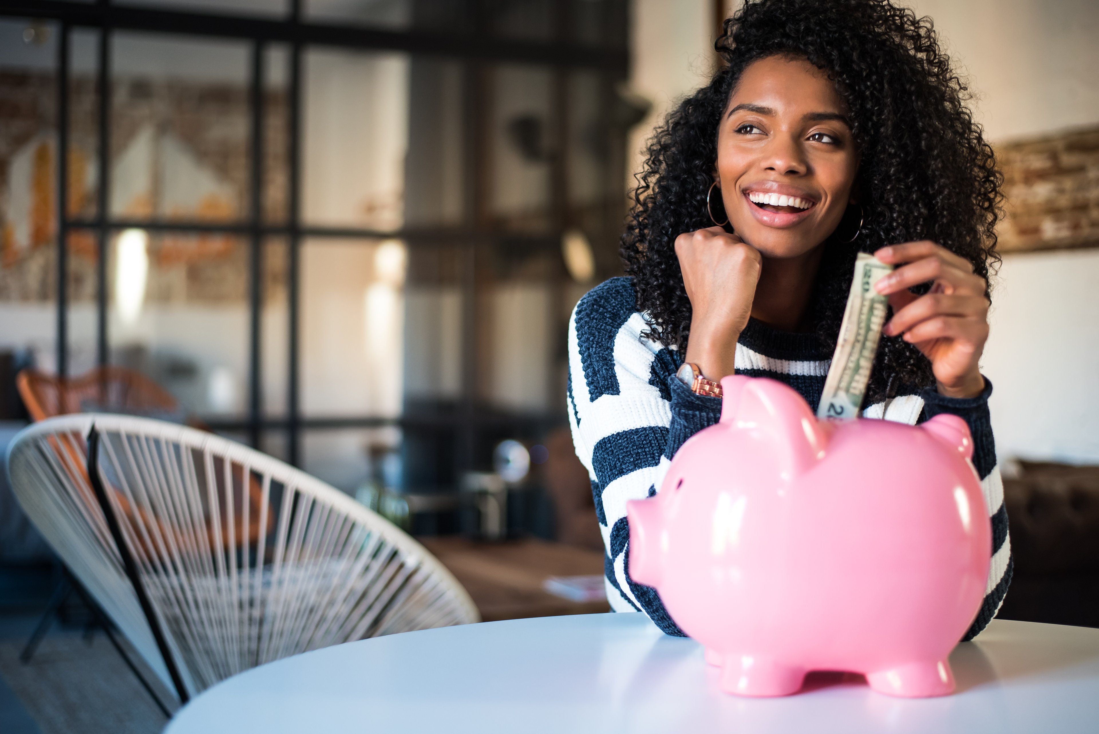 A woman sits at a table and puts a large bill in a piggy bank