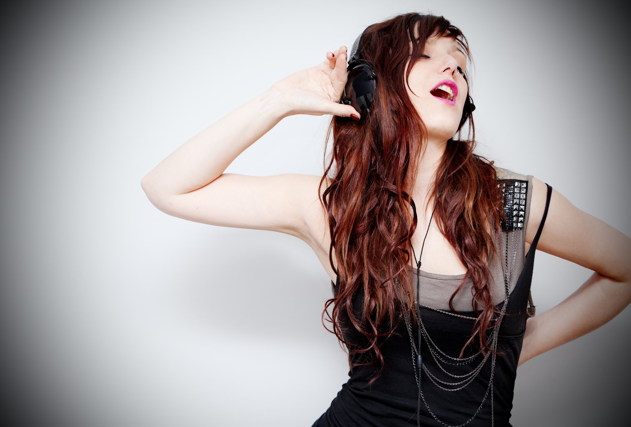 A smiling young woman with headphones dances with one hand cupped to her ear.