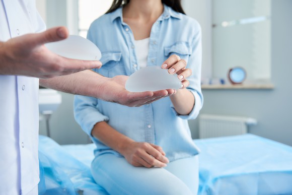 Woman receiving consultation in a clinic while a doctor holds a pair of silicon breast implants.