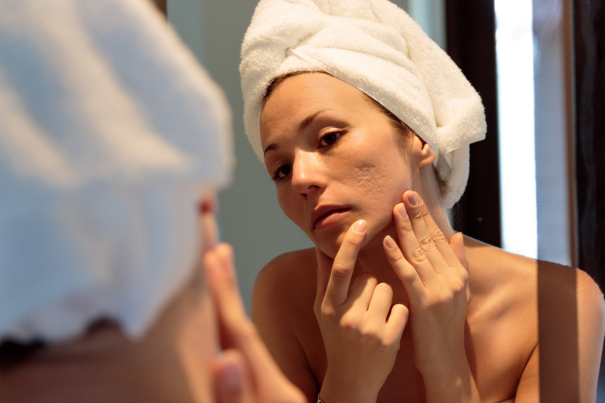 Woman wearing towel examines face in mirror