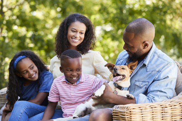 A man holds a small dog while his wife and two kids look on, smiling.