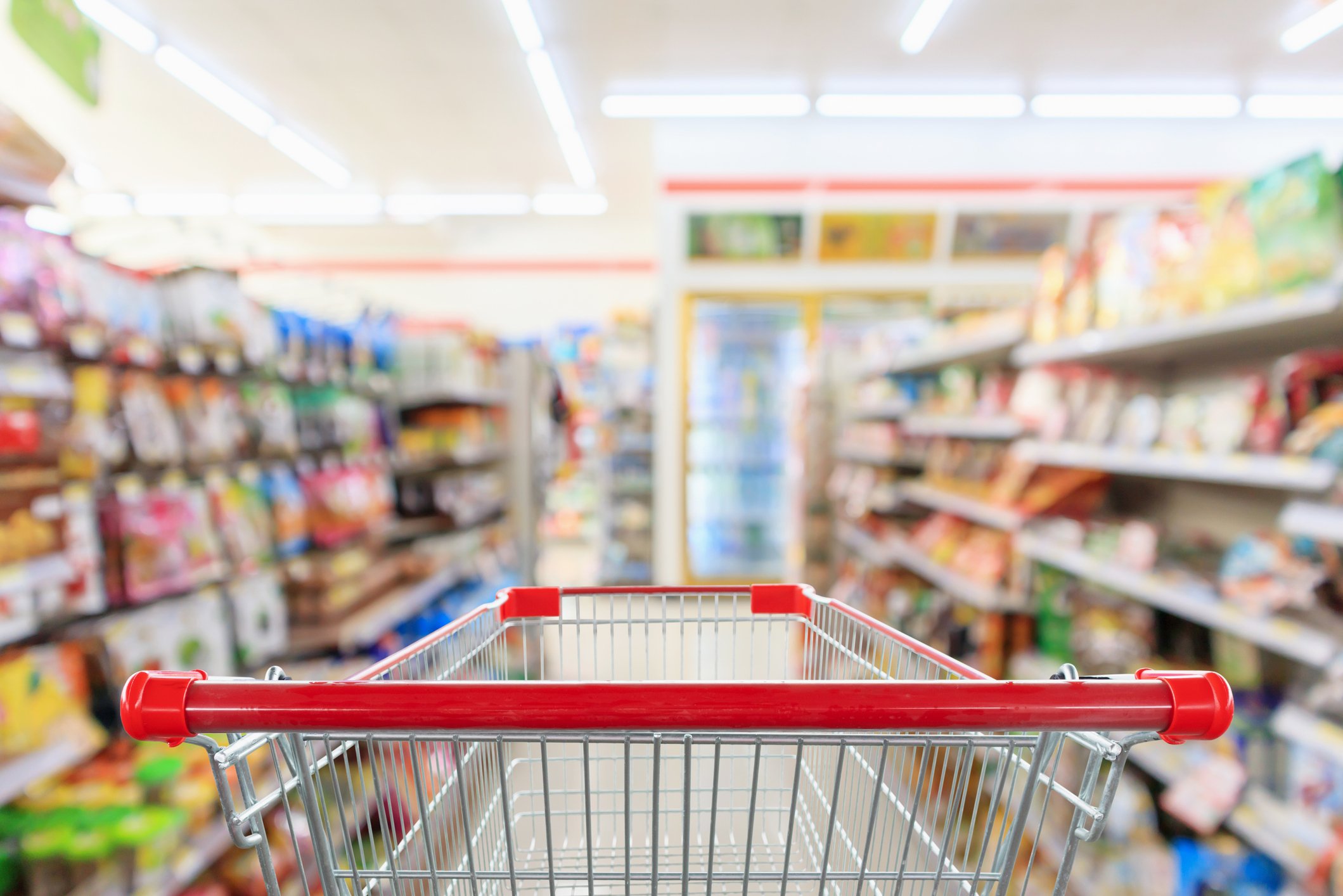 Shopper's-eye view of a grocery shopping cart at the head of a store aisle.