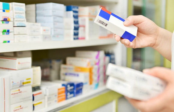 Hands taking medication from a pharmacy shelf