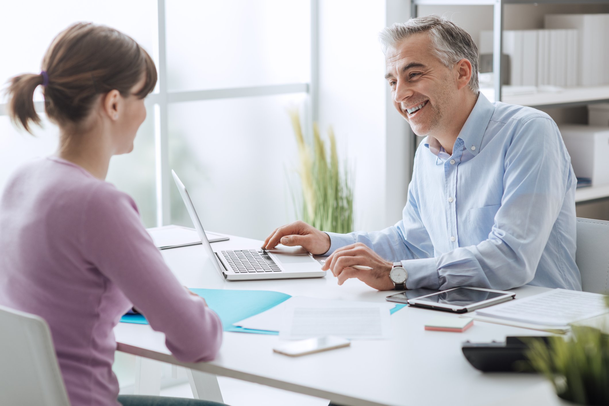 Woman seated across from smiling professionally dressed man at a laptop