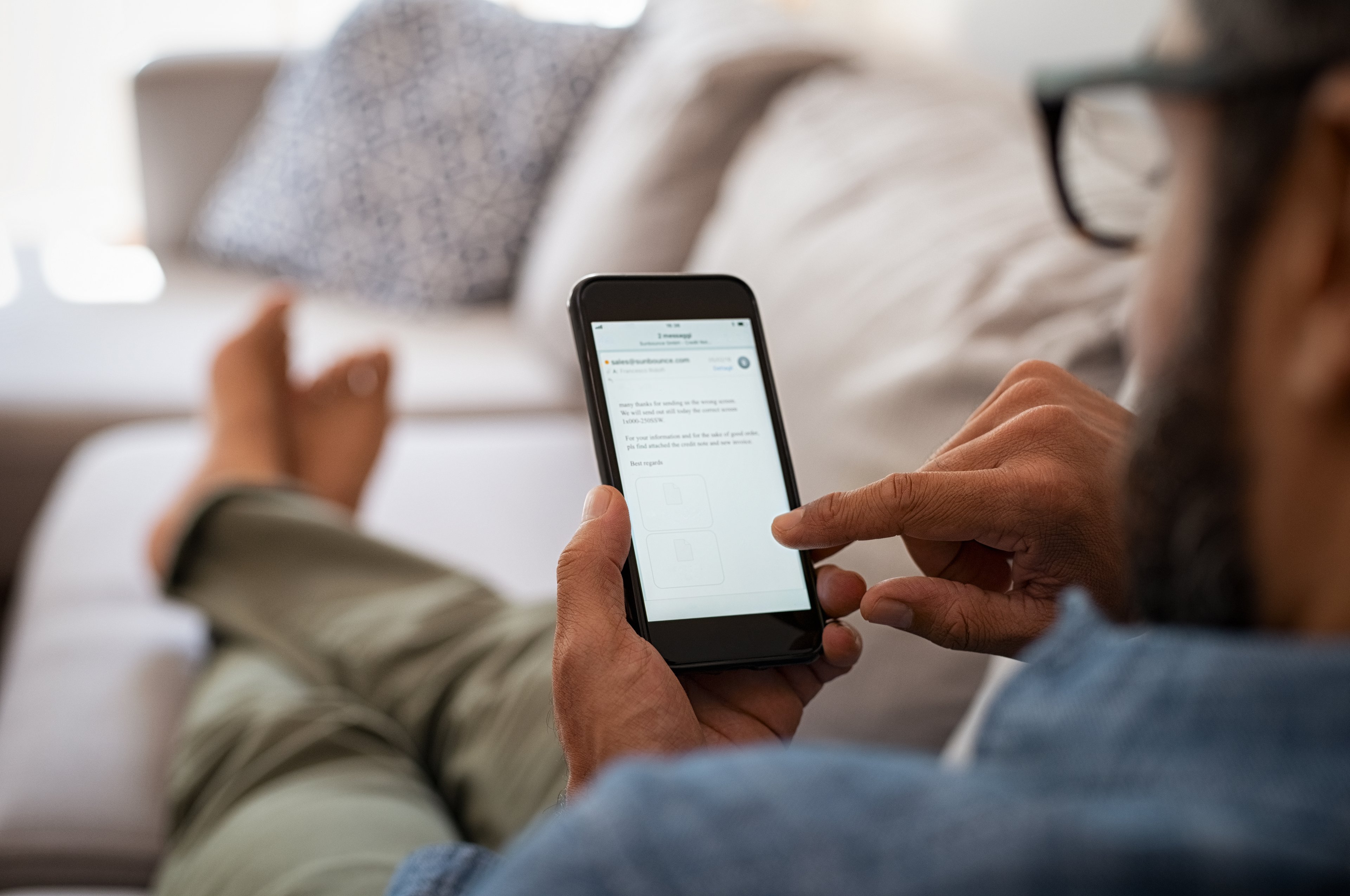 A man using his smartphone sitting on a couch with the screen illuminated