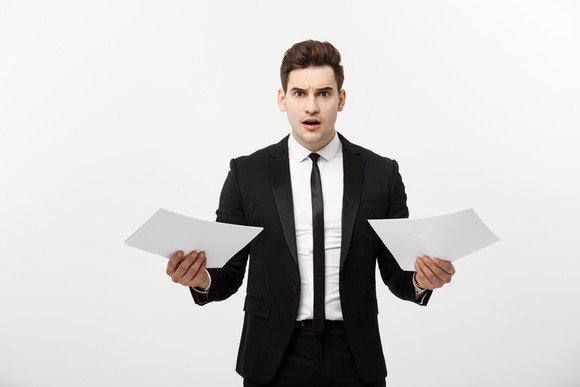 A businessman holding up two pieces of paper with a worried look on his face.