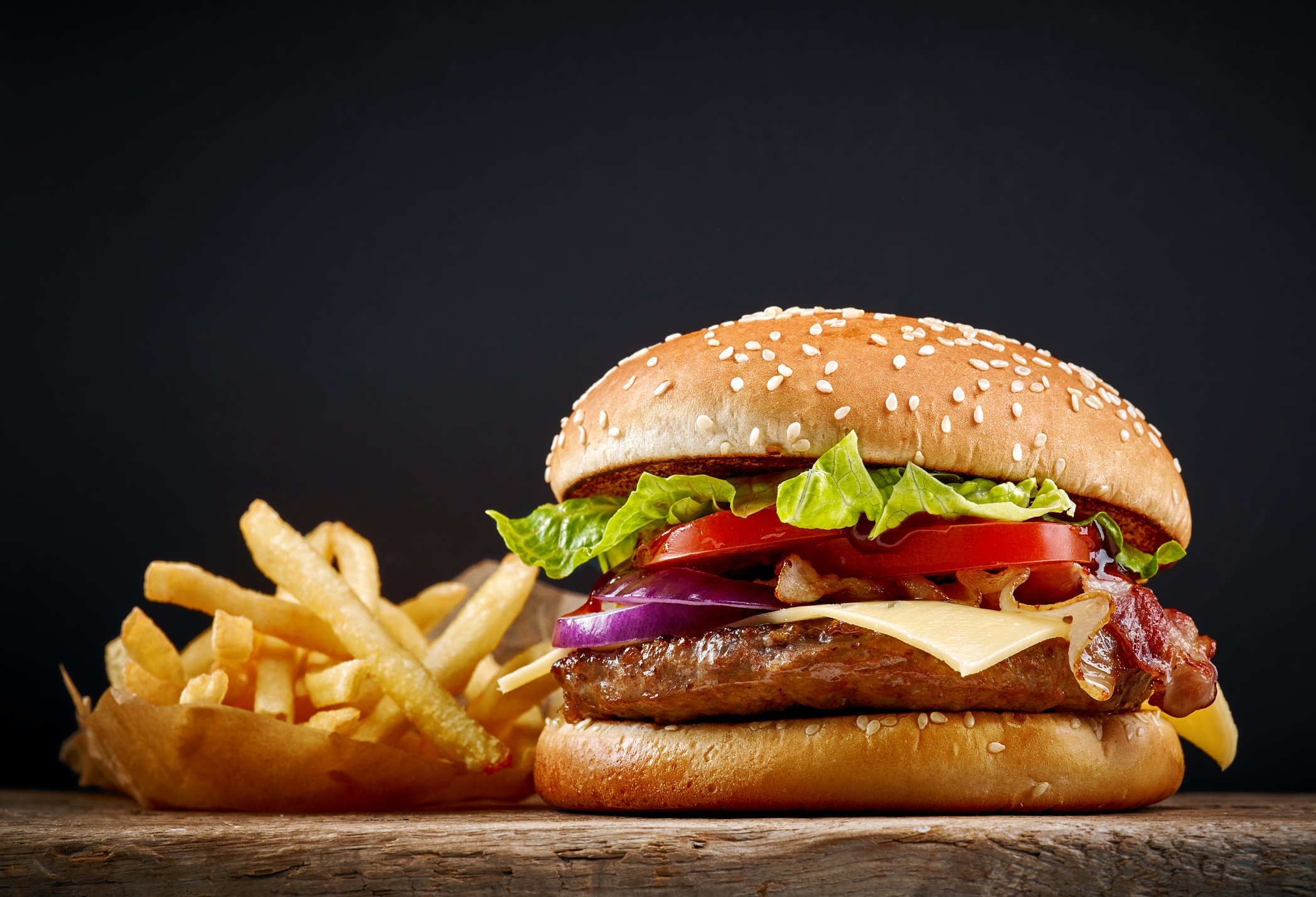 A juicy hamburger with fries on a chopping board.
