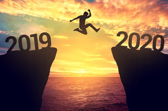 A person leaping from one rock to another. The number 2019 is on the one he's leaving and 2020 is on the one he is headed to.