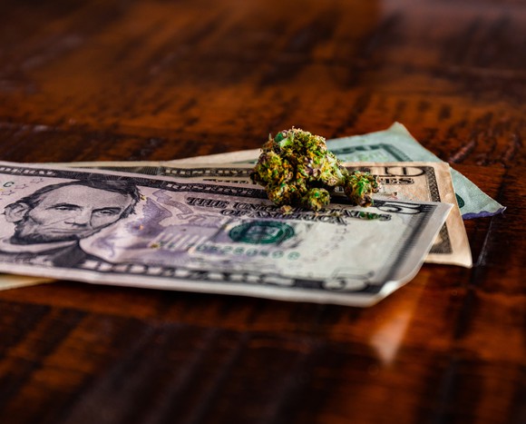 Cannabis buds lying on a pile of cash on a table.