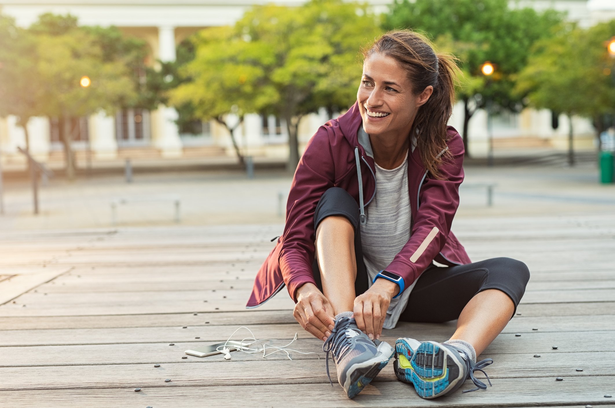 A smiling woman sitting outside while putting on sneakers.