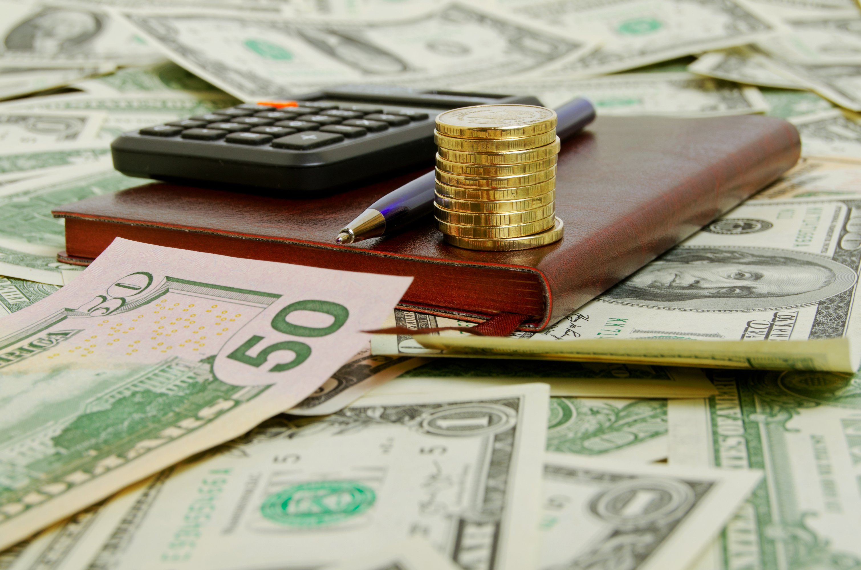 Calculator, book, and pen on top of a pile of money.