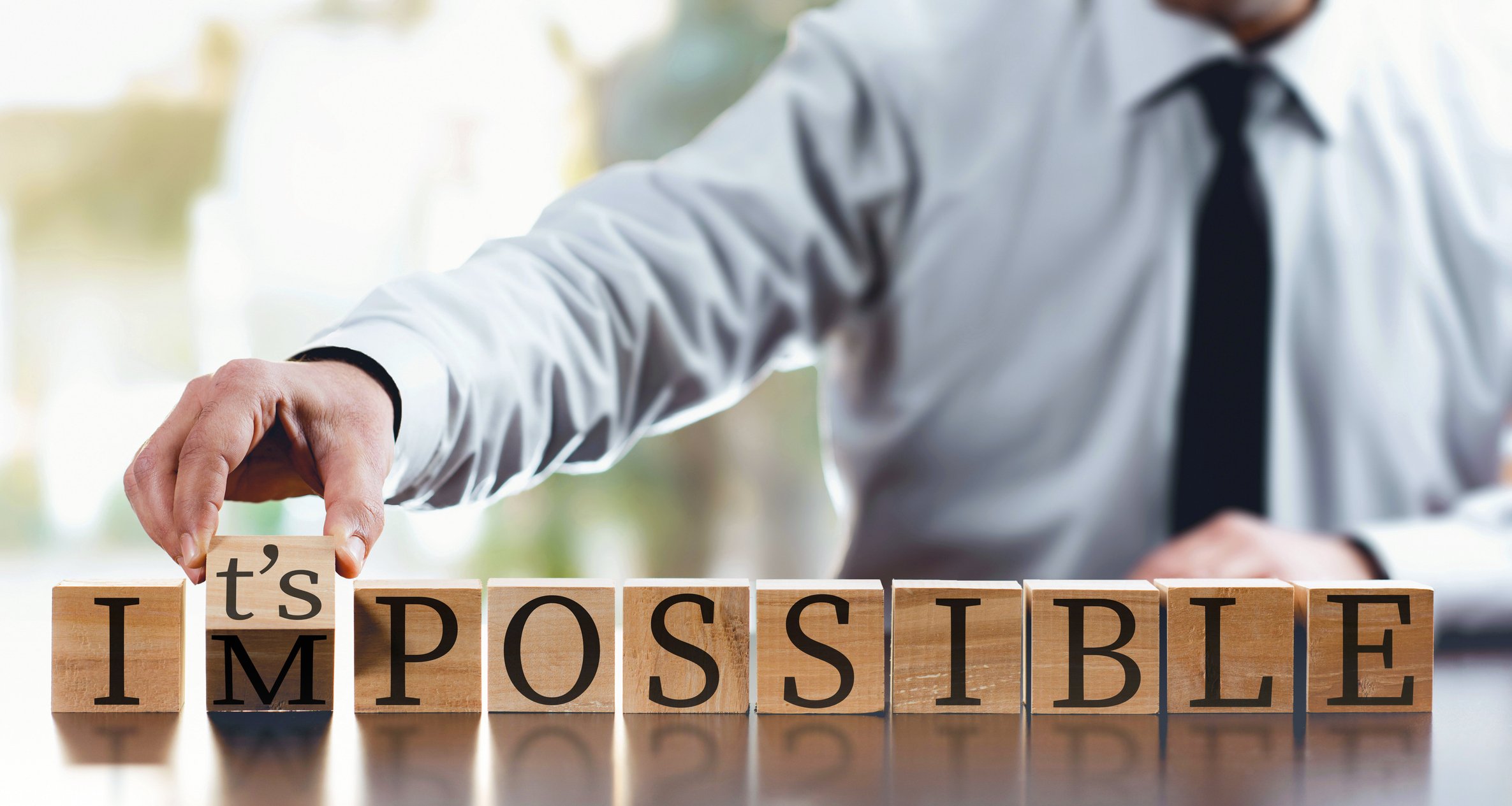 A series of wood blocks spells out the word impossible. A man turns over the M block to make the blocks spell the words it's possible.
