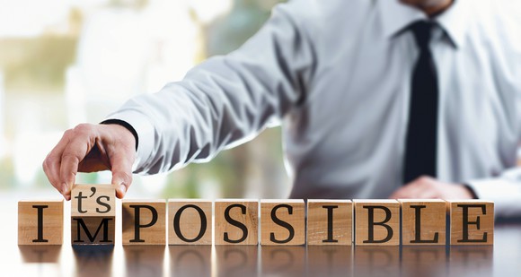 A series of wood blocks spells out the word impossible. A man turns over the M block to make the blocks spell the words it's possible.