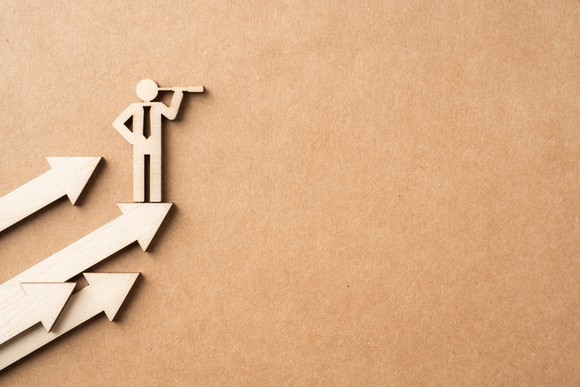 A wooden businessman standing on rising arrows and looking into the distance.