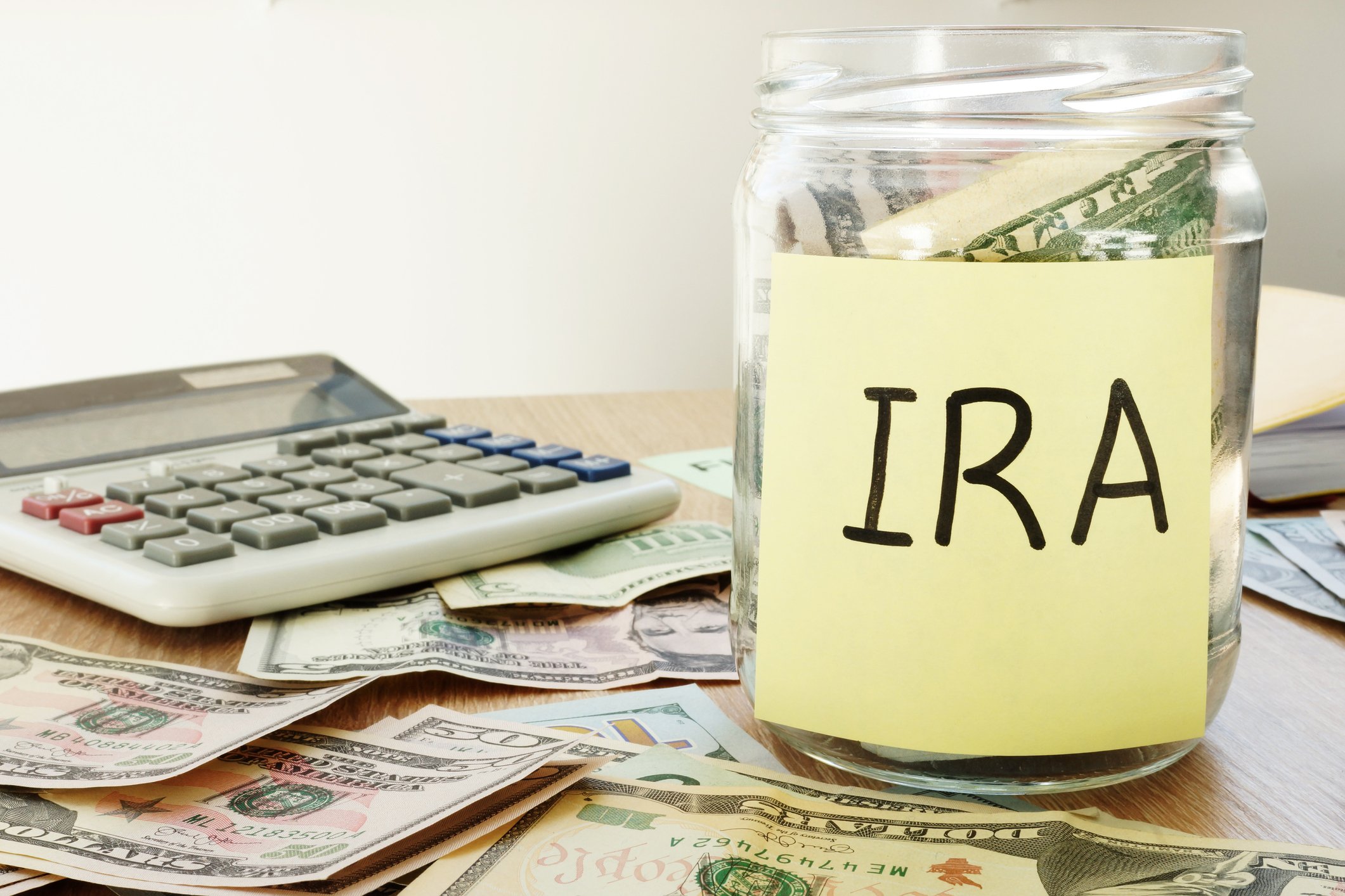Money jar labeled IRA with cash on the desk around it.