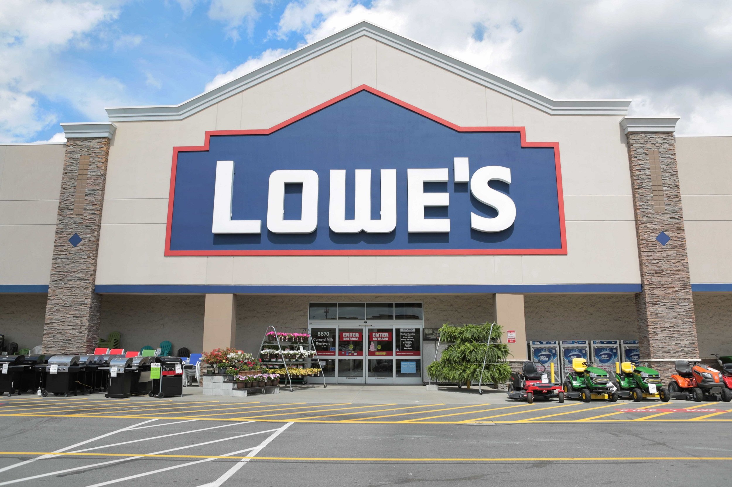 Lowe's storefront with lawn mowers parked on sidewalk.