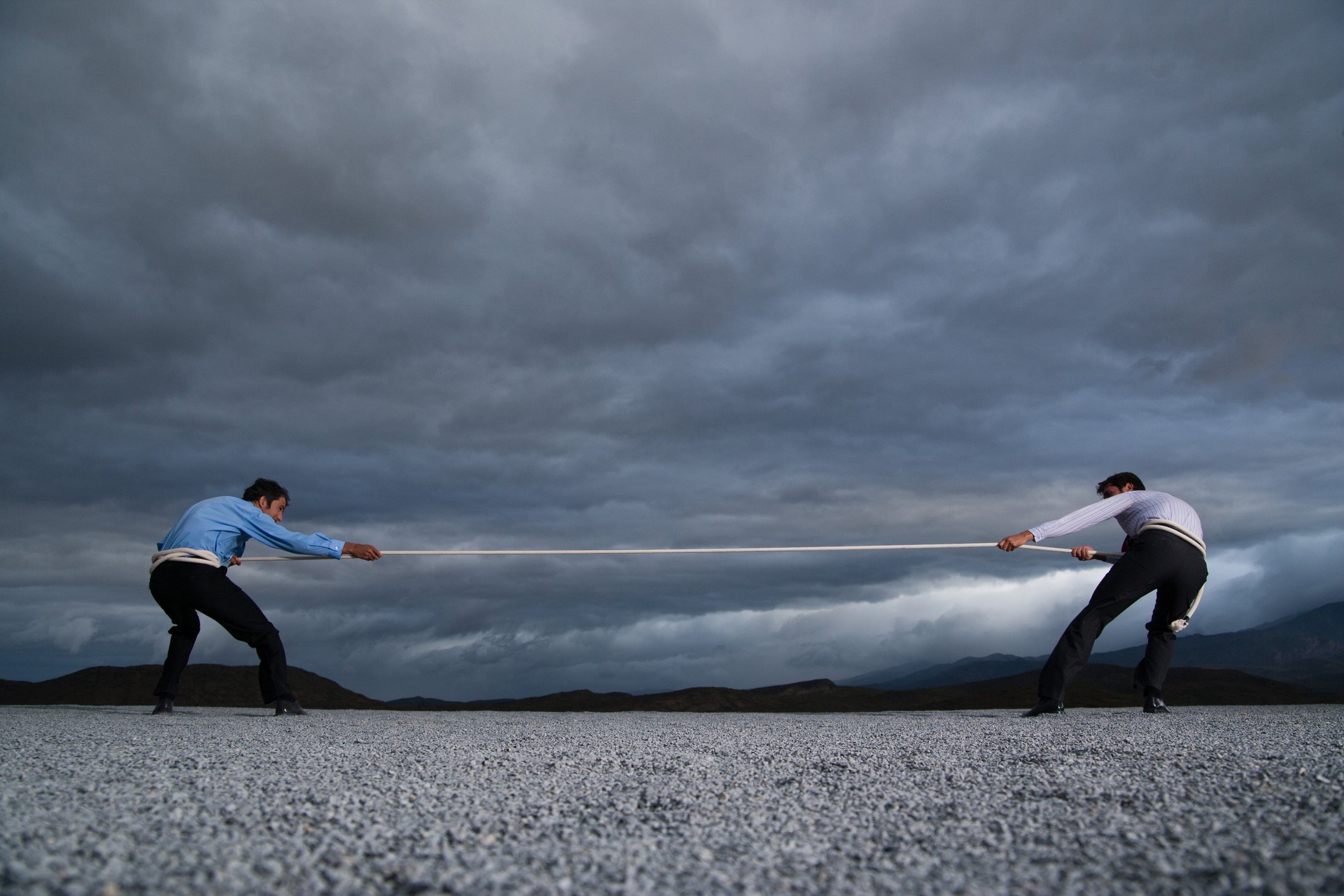 Two men pulling on opposite sides of rope in front of a dramatic landscape