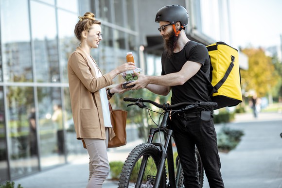 A food delivery person on a bike giving a salad and beverage to a woman
