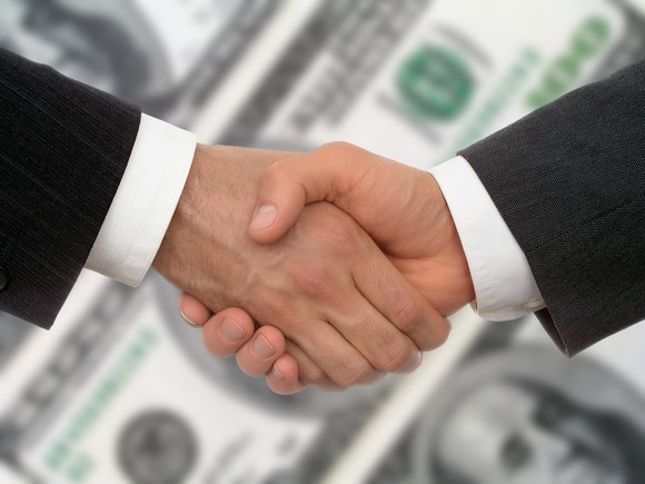Two men shaking hands, with hundred dollar bills in the background.