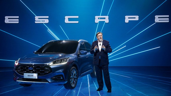 A man standing next to a blue Ford Escape SUV on a blue stage. 