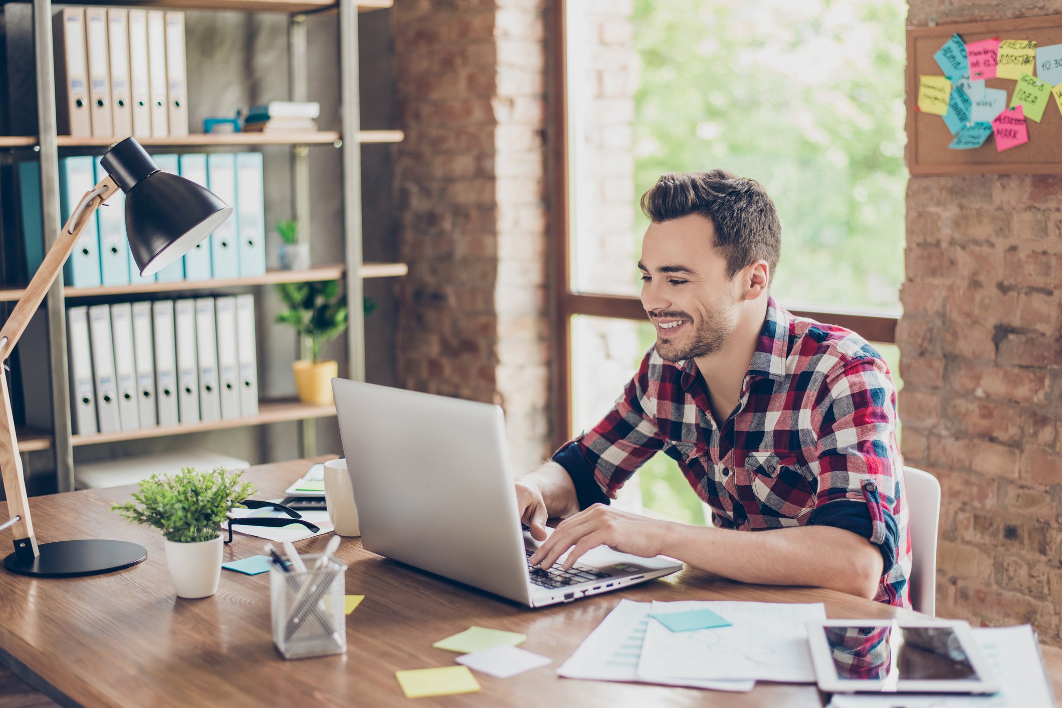Smiling man typing on laptop in front of window