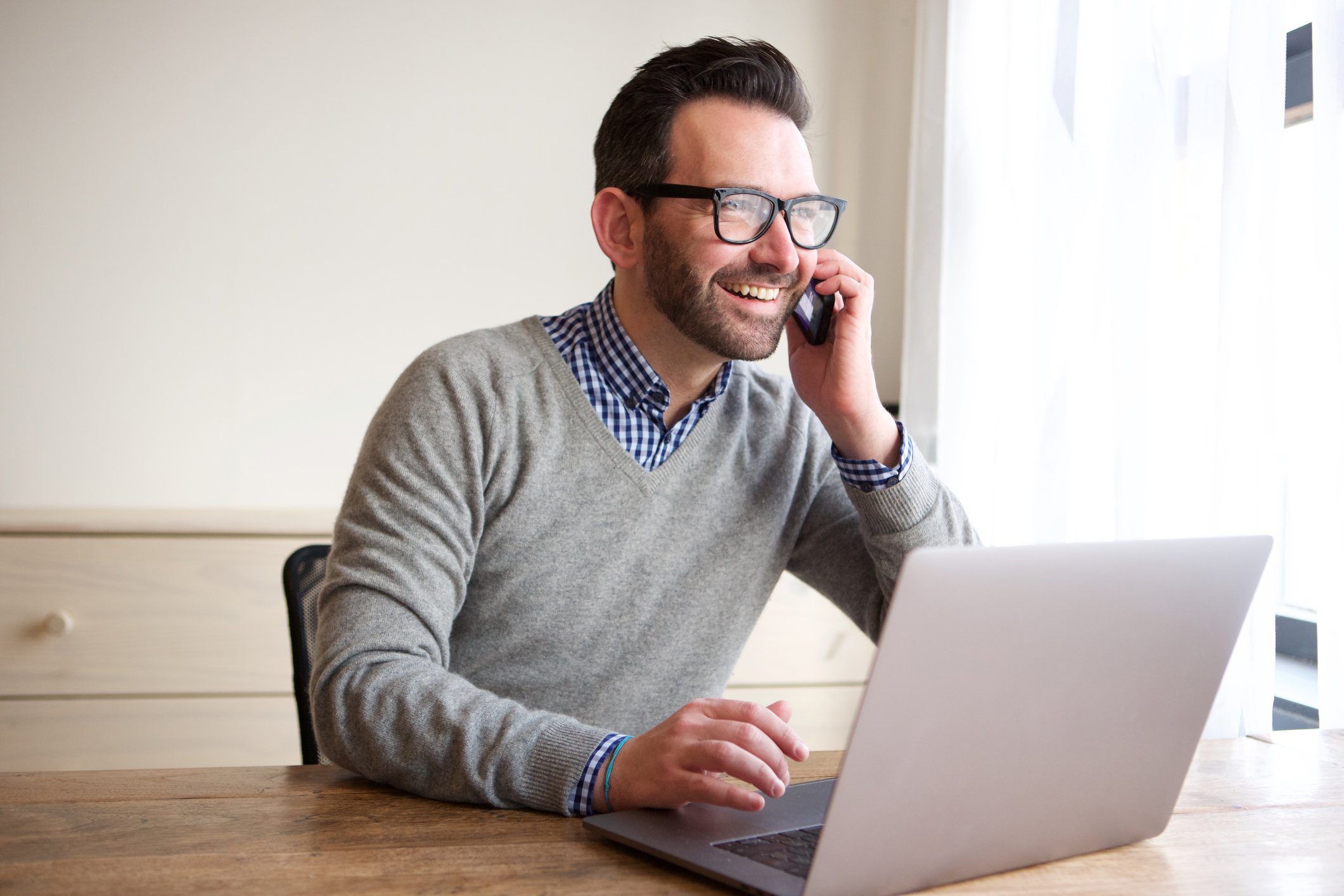 Smiling man at laptop talking on phone