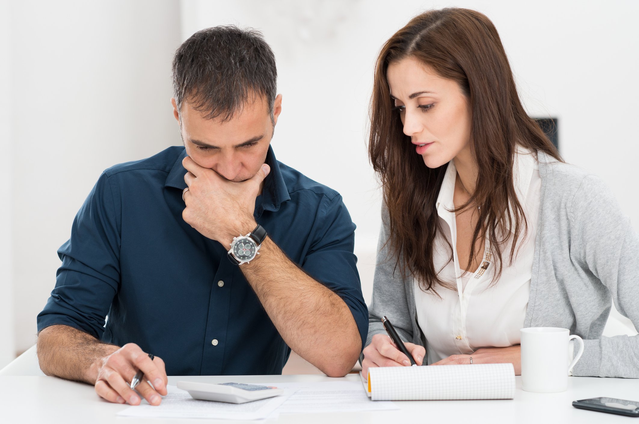 Man looks down at calculator while woman writes in notebook
