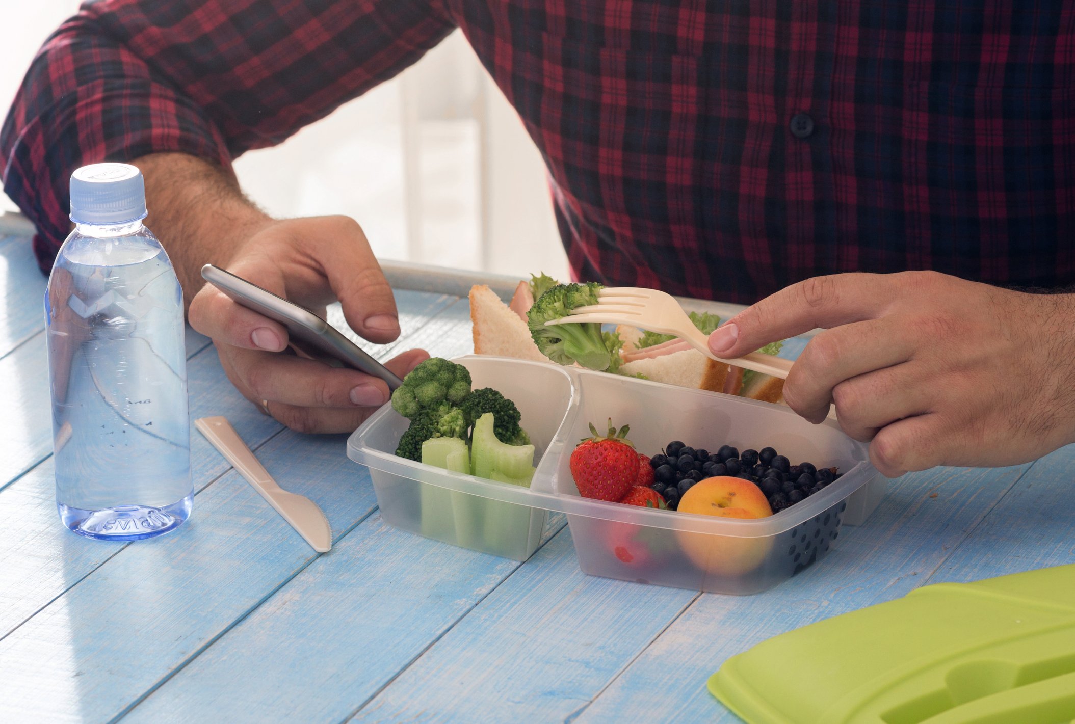 A man eating a meal from a to-go box with a bottle of water beside it.