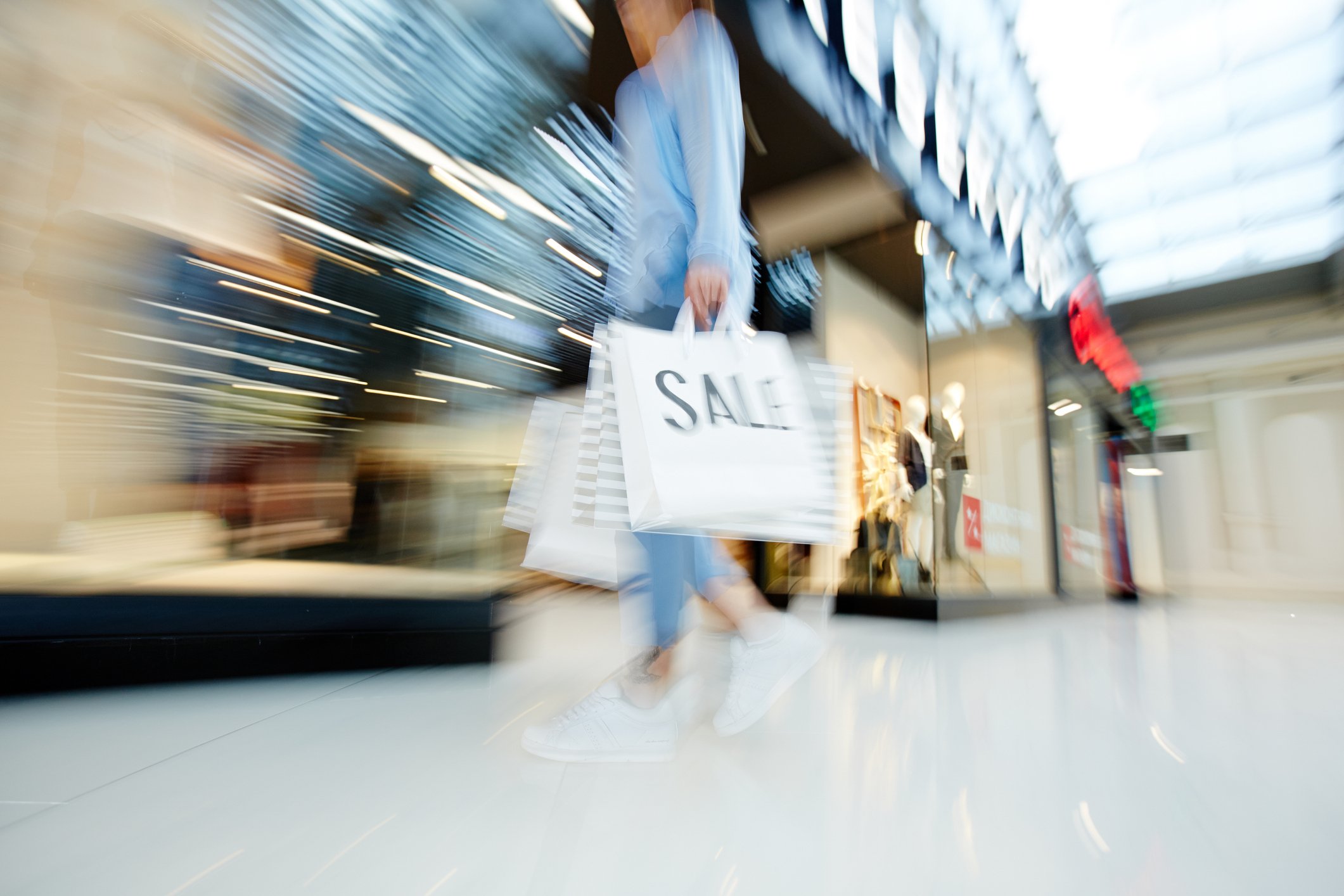A blurred image reveals a woman holding shopping bags as she walks through a store.