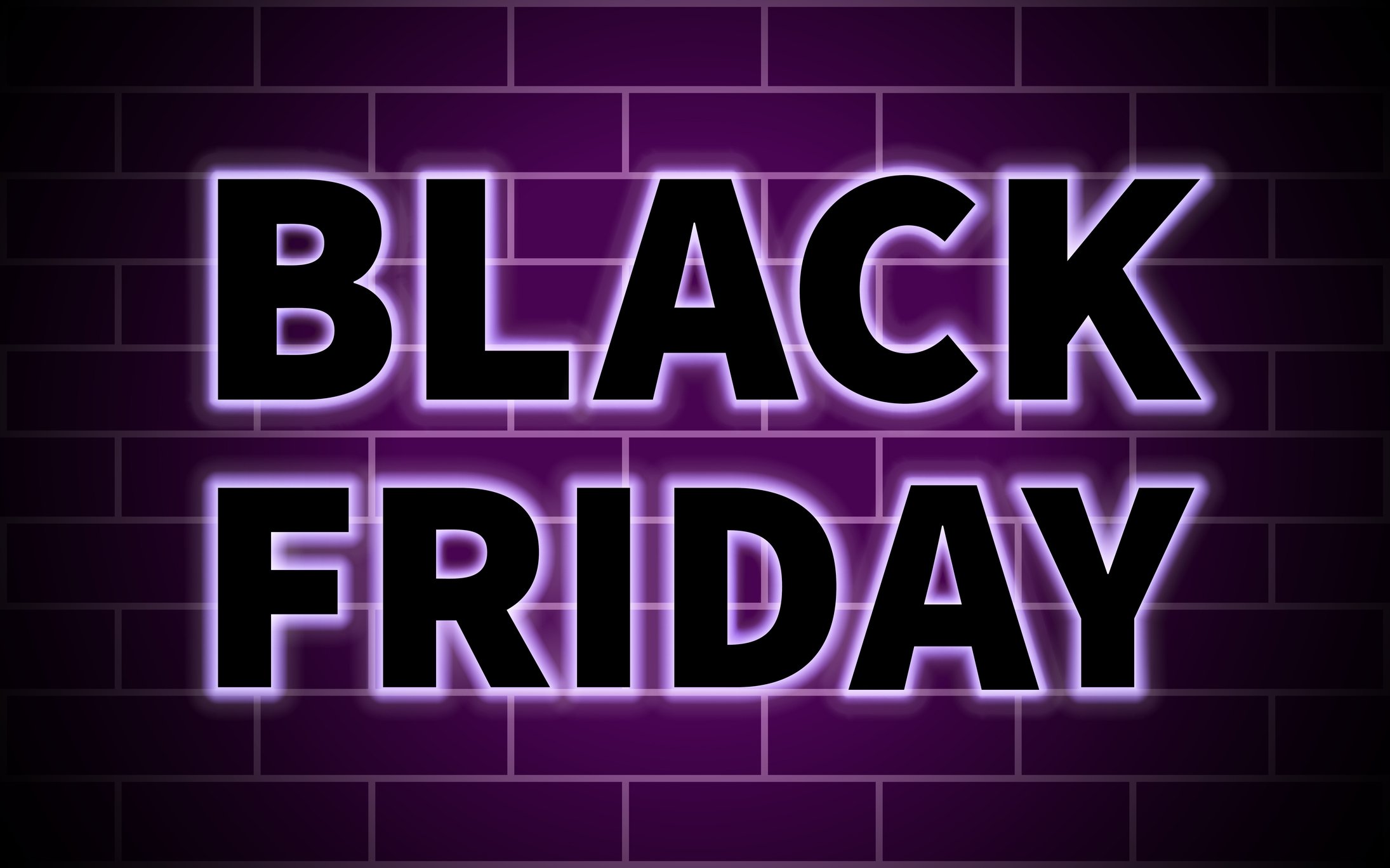 The words Black Friday in purple neon against a brick wall.