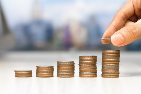 A hand stacks a coin on ascending towers of coins.