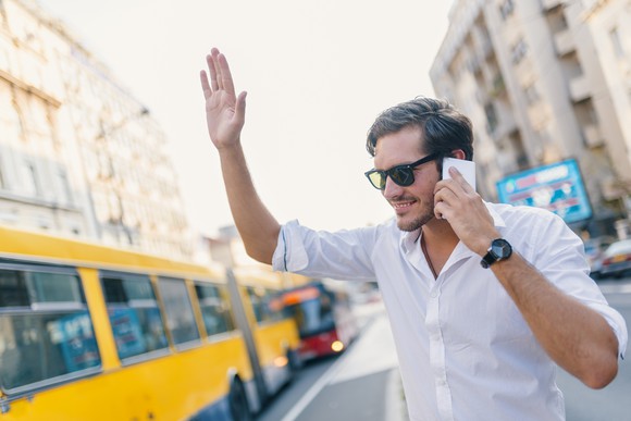 Young guy in sunglasses on his phone and hailing his ride. 