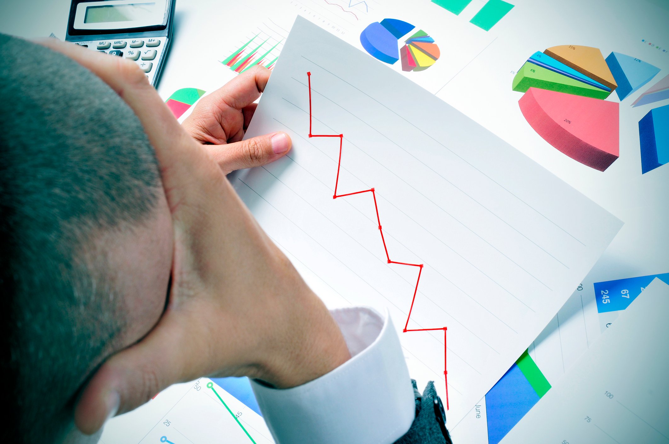 Man with hand on head looking at charts with a line chart trending downward.