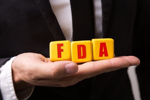Person in a suit holding three blocks that spell FDA.