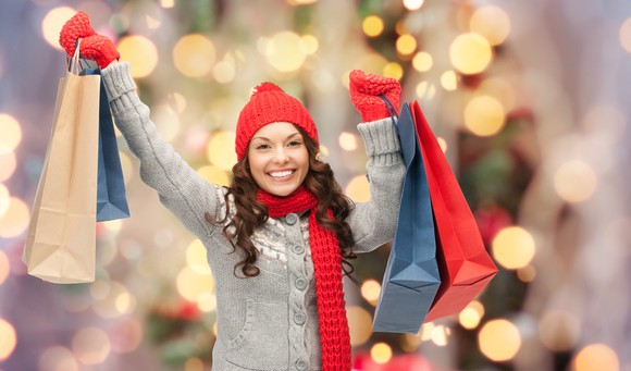 A woman in winter clothes holding up several shopping bags