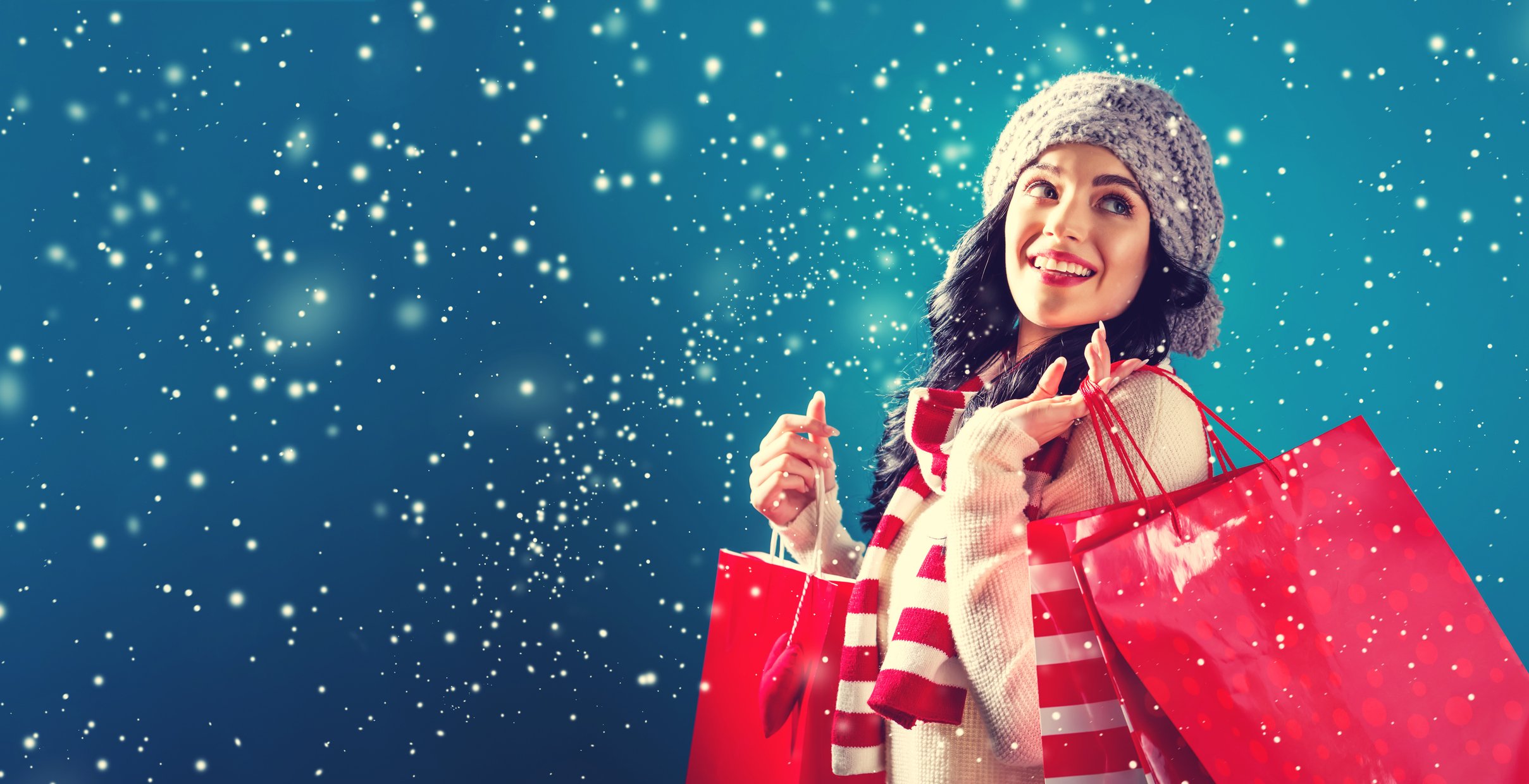 Smiling woman holding shopping bags while it snows.
