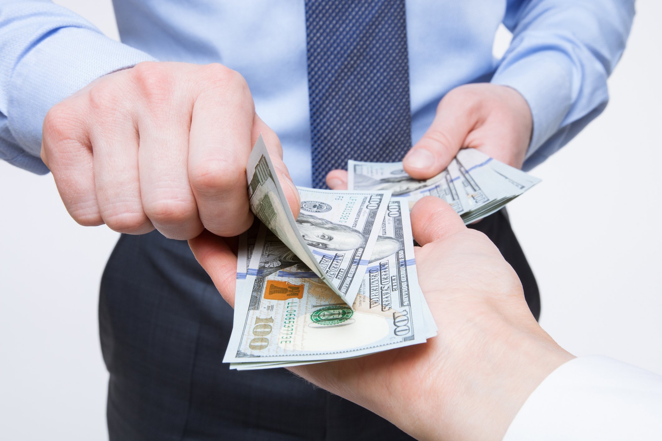 A man in a dress shirt and tie counting out $100 bills into another man's hand.