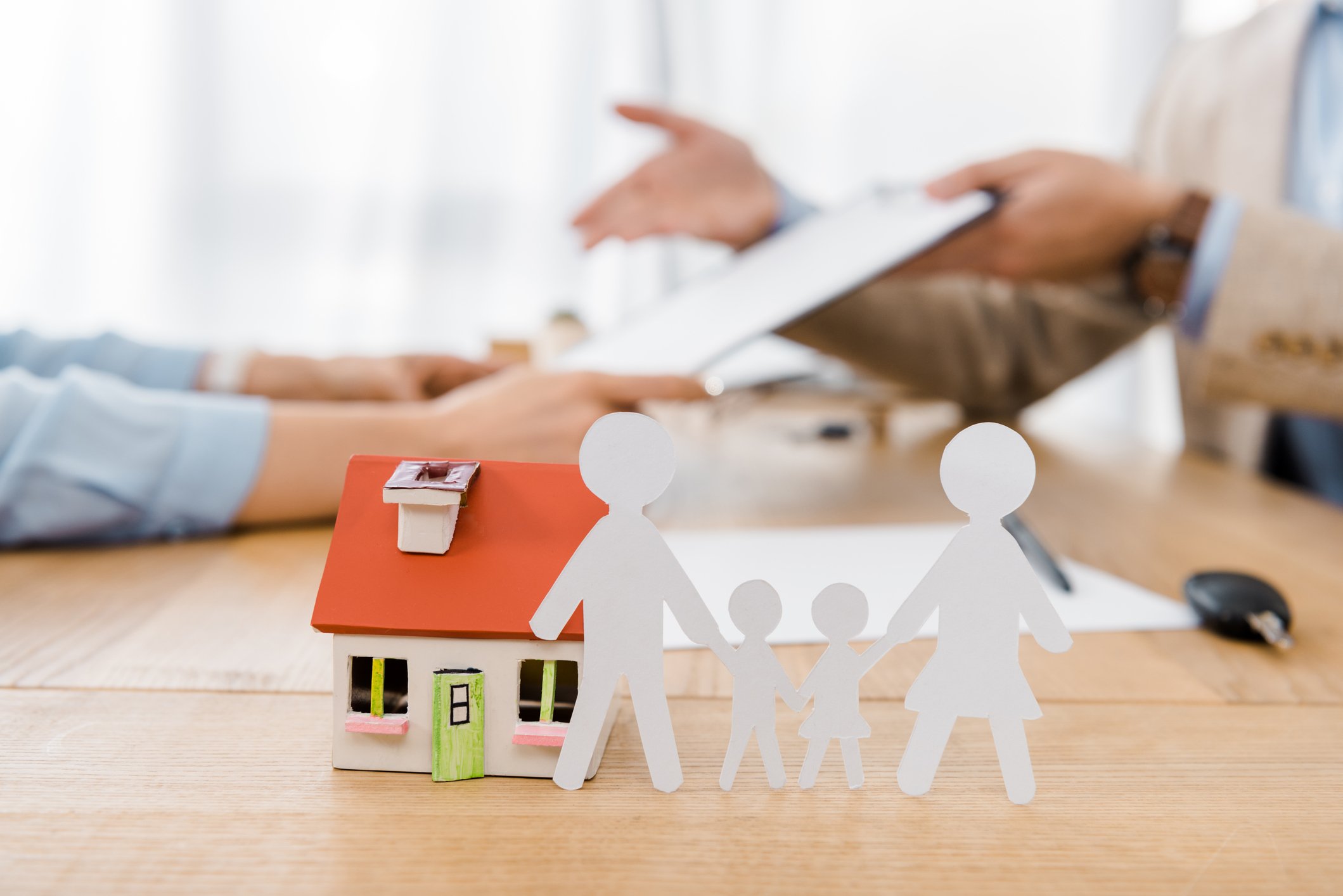 Person signing life insurance contract with a toy house and family of paper dolls in the foreground.