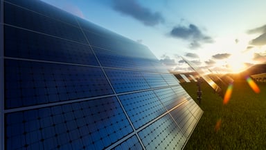 Solar panels with the sun shining over a hill.