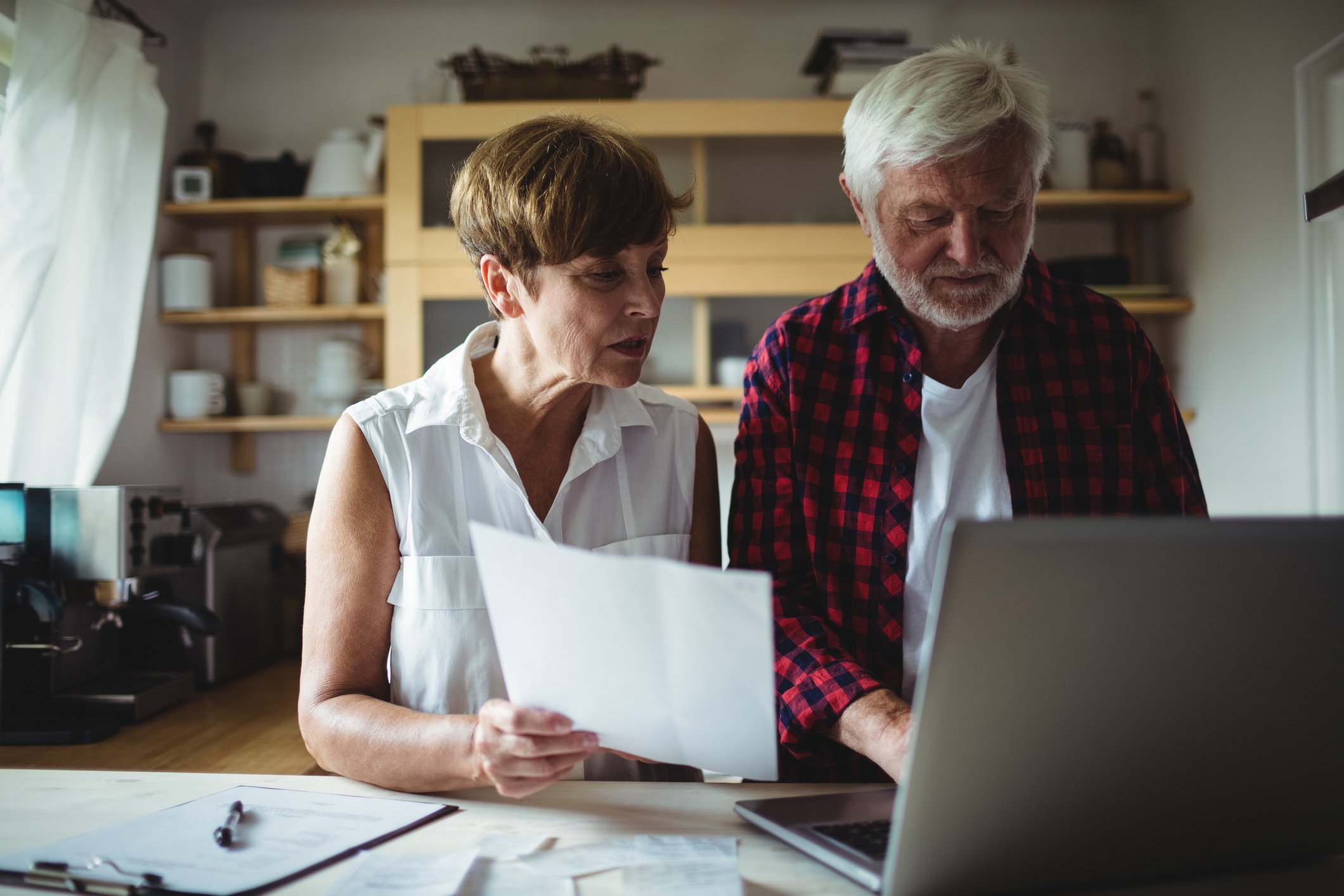 Older woman holds document and looks on while older man types on laptop