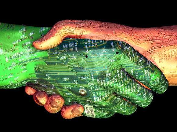 Two hands executing a handshake. Both are covered in circuit-board traces, one of them is also green.