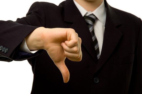 A person in a business suit making a thumbs-down gesture.