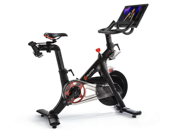 A Peloton stationary bike with a live-streamed workout on the attached monitor.