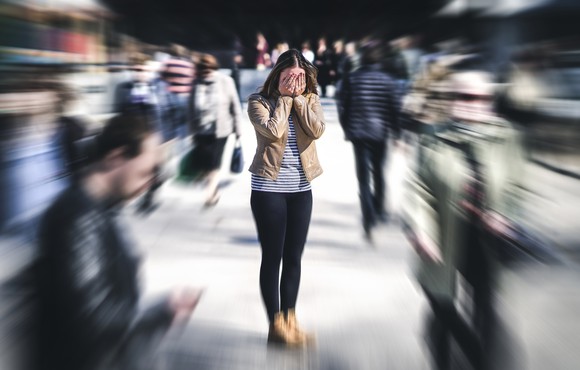 A woman stands with her hands over her face on a crowded sidewalk.
