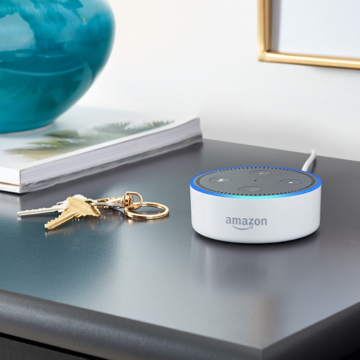 The Echo Dot on an end table next to keys and a lamp.