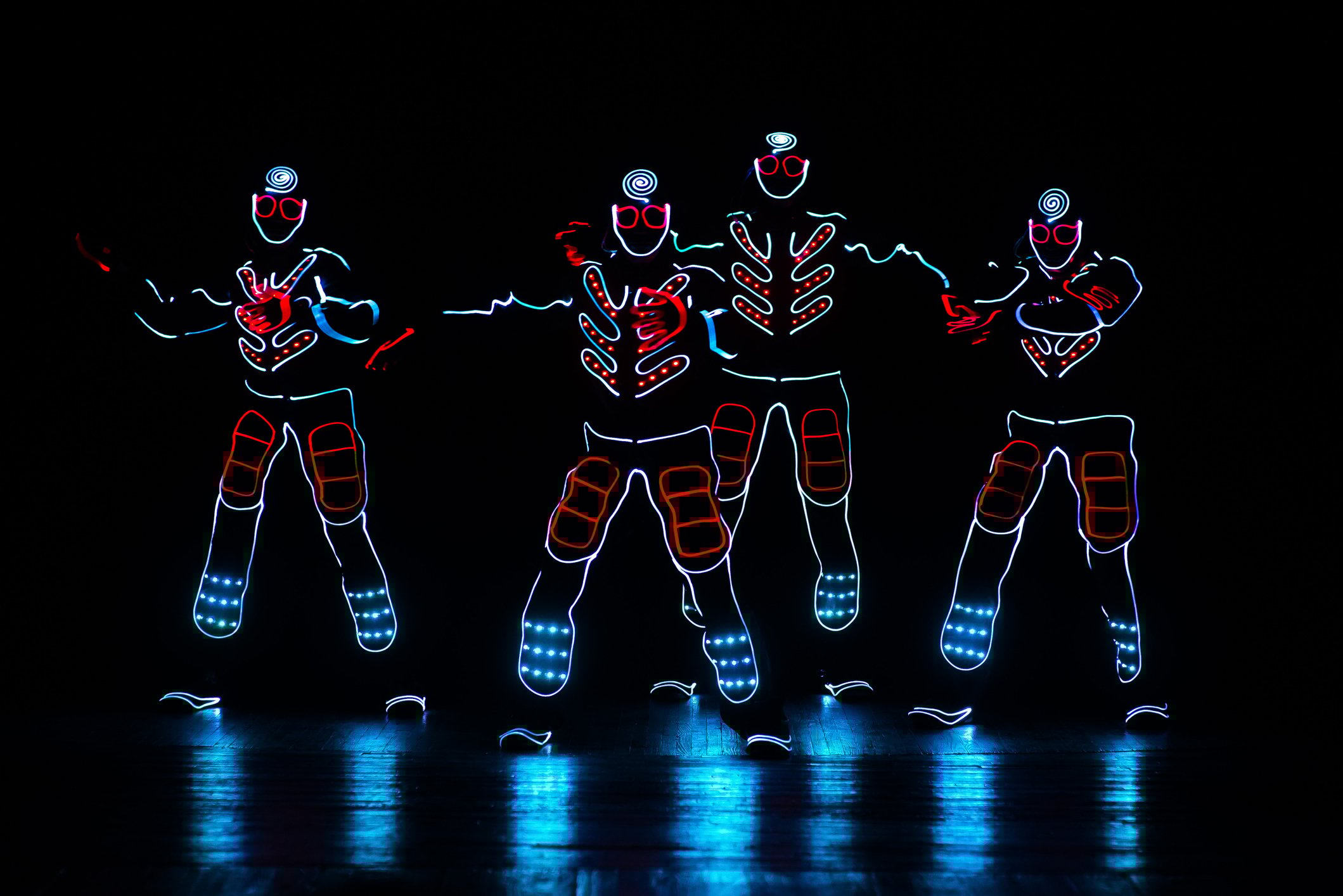 Four glowing figures on a dark stage.