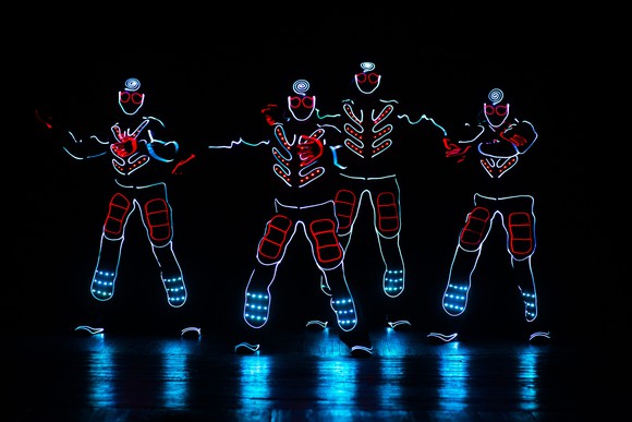 Four glowing figures on a dark stage.