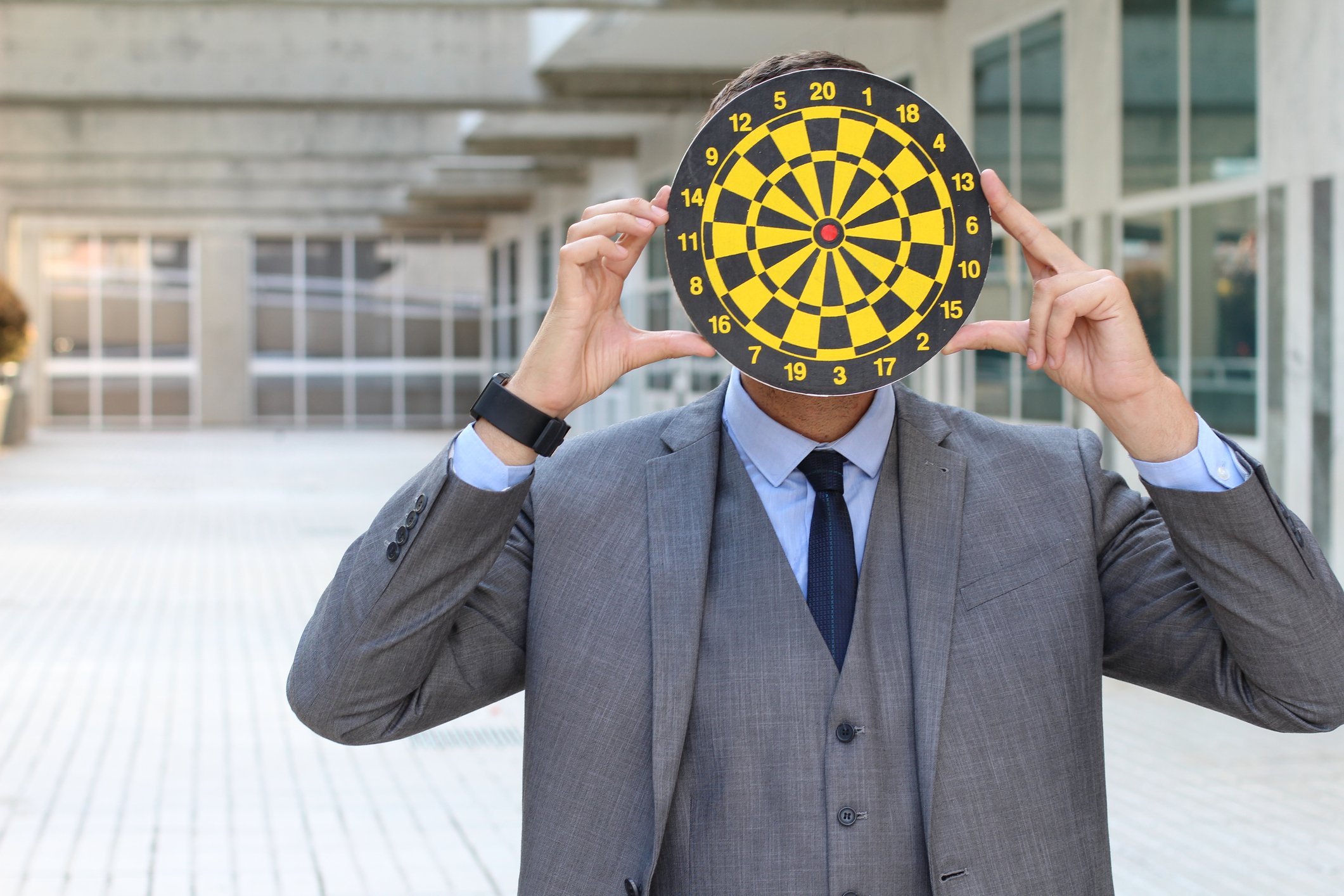 A businessman holds a dartboard in front of his face.